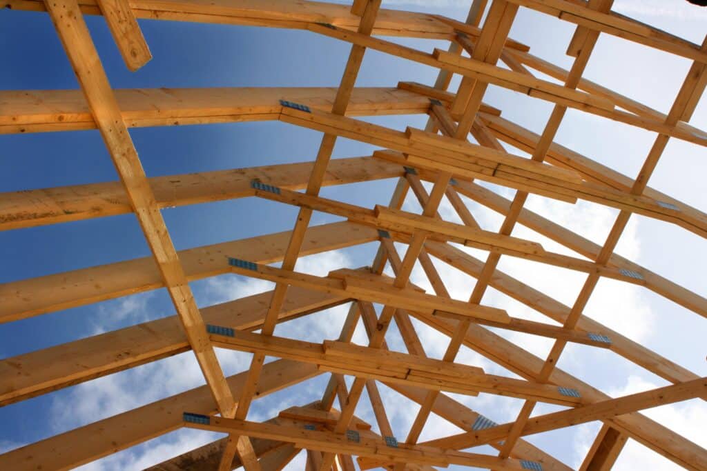 Charpente en bois d'un toit en construction, vue d'en bas, avec des fermes et des connecteurs métalliques sur fond de ciel bleu.