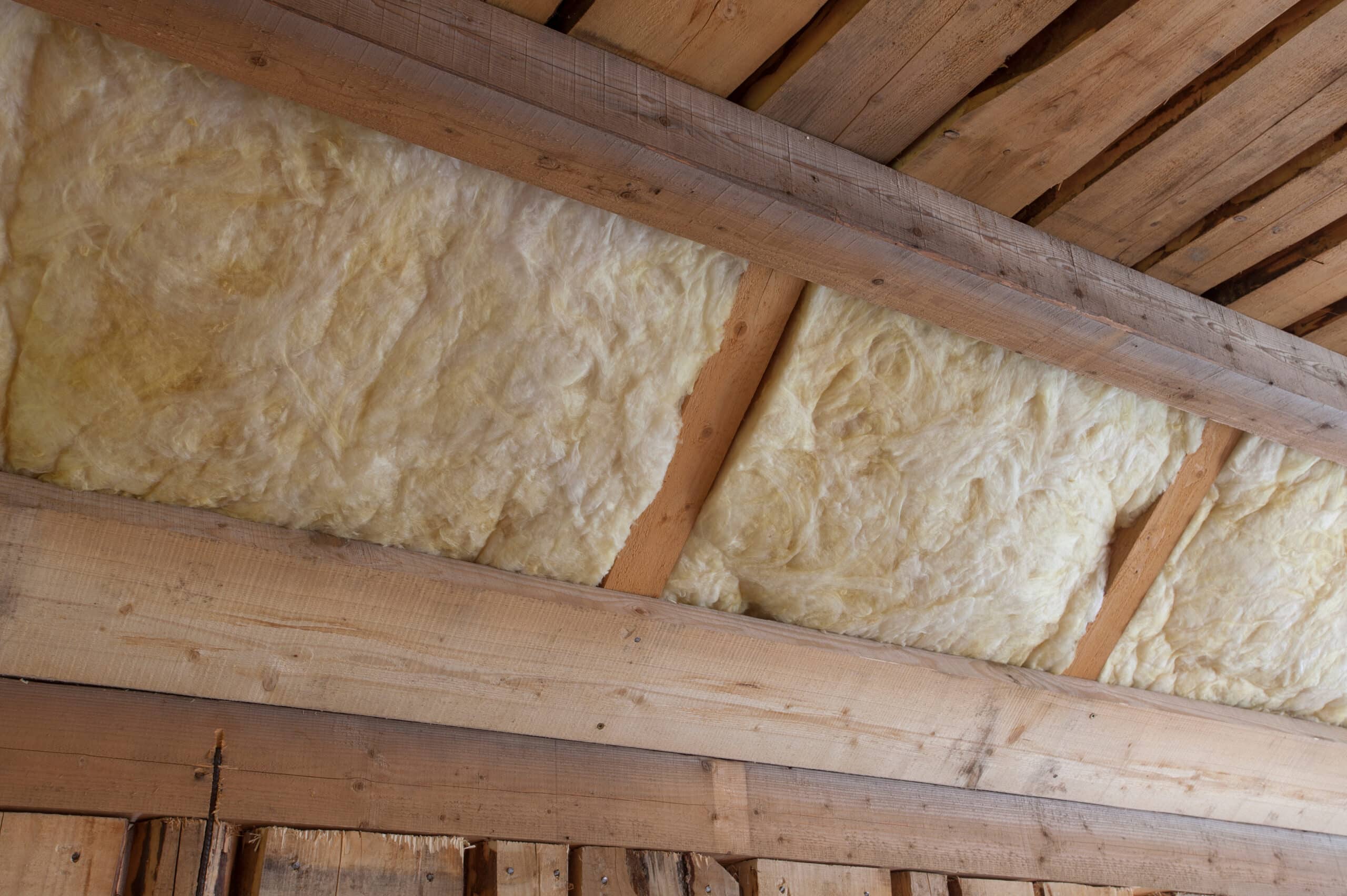 Laine minérale jaune installée entre des poutres et planches de bois brut, isolant une structure de toit ou de grenier.